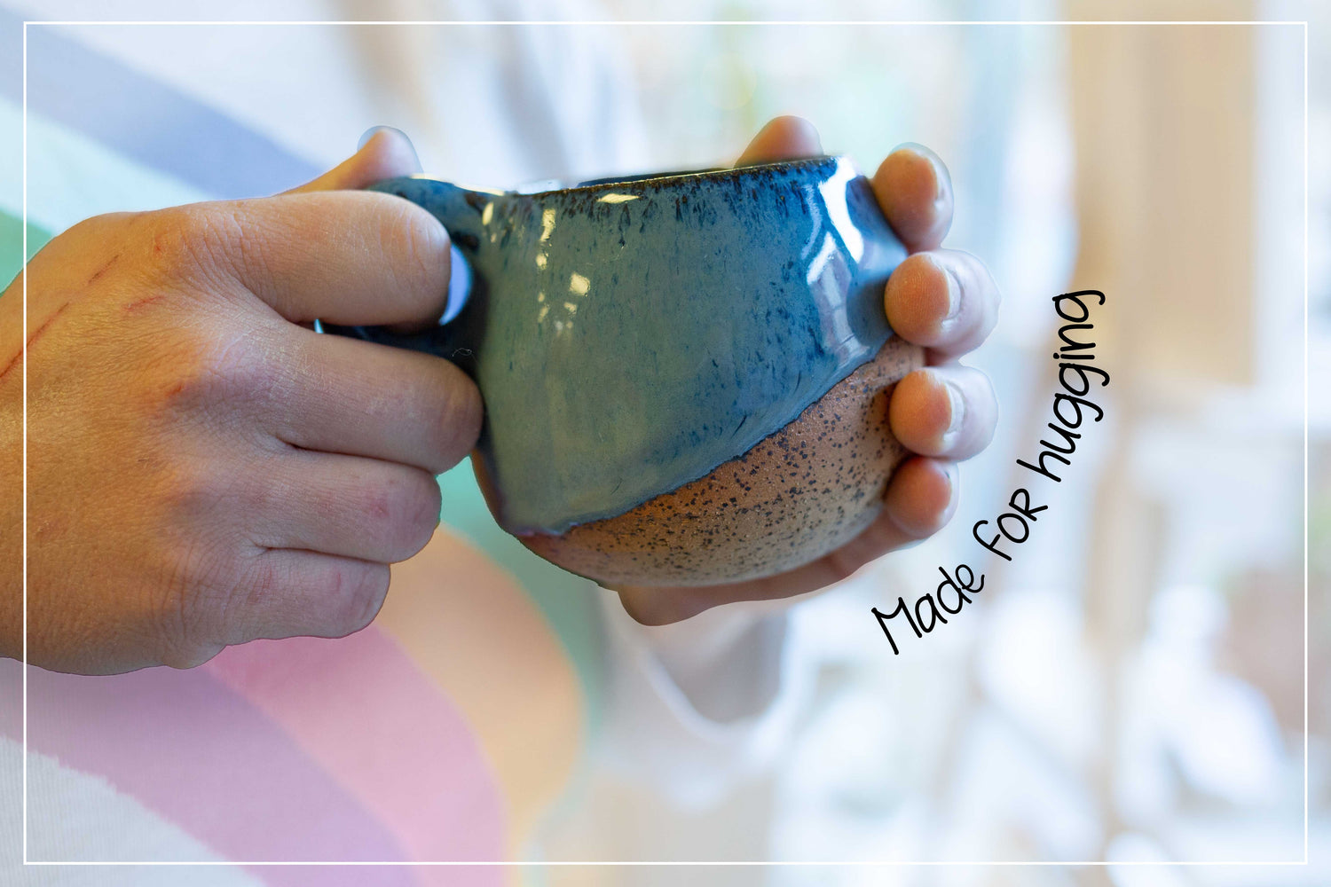 Hand holding a blue ceramic mug with text 'Made for hugging' on a blurred background